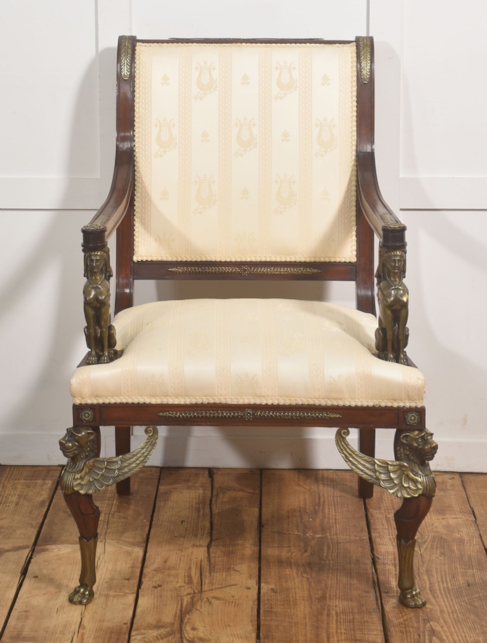 An Empire style mahogany armchair featuring cream upholstered silk fabric with lyre motifs, winged sphinx arm supports, and gilt brass winged lion front legs. View VII