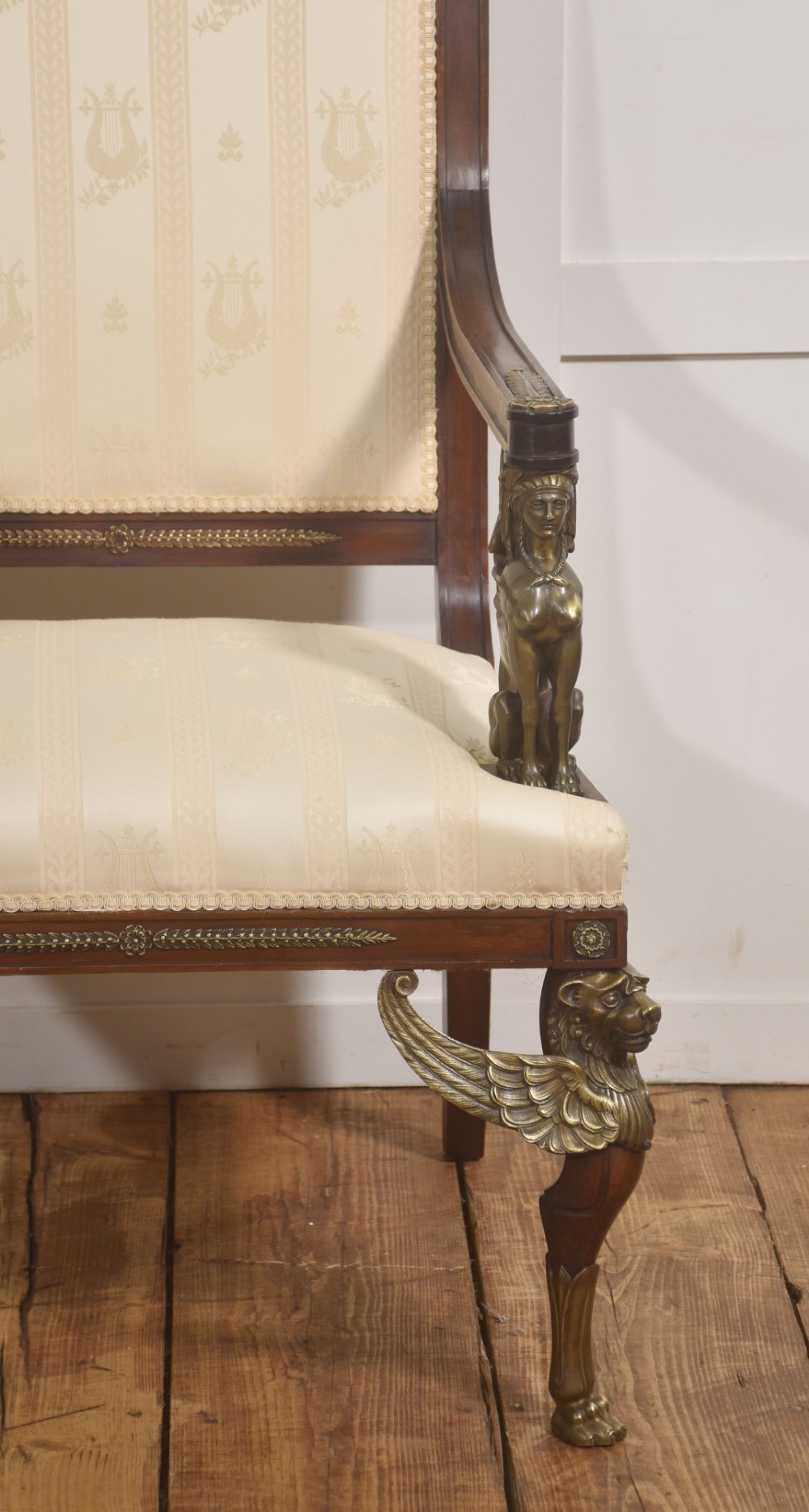 An Empire style mahogany armchair featuring cream upholstered silk fabric with lyre motifs, winged sphinx arm supports, and gilt brass winged lion front legs. View VIII