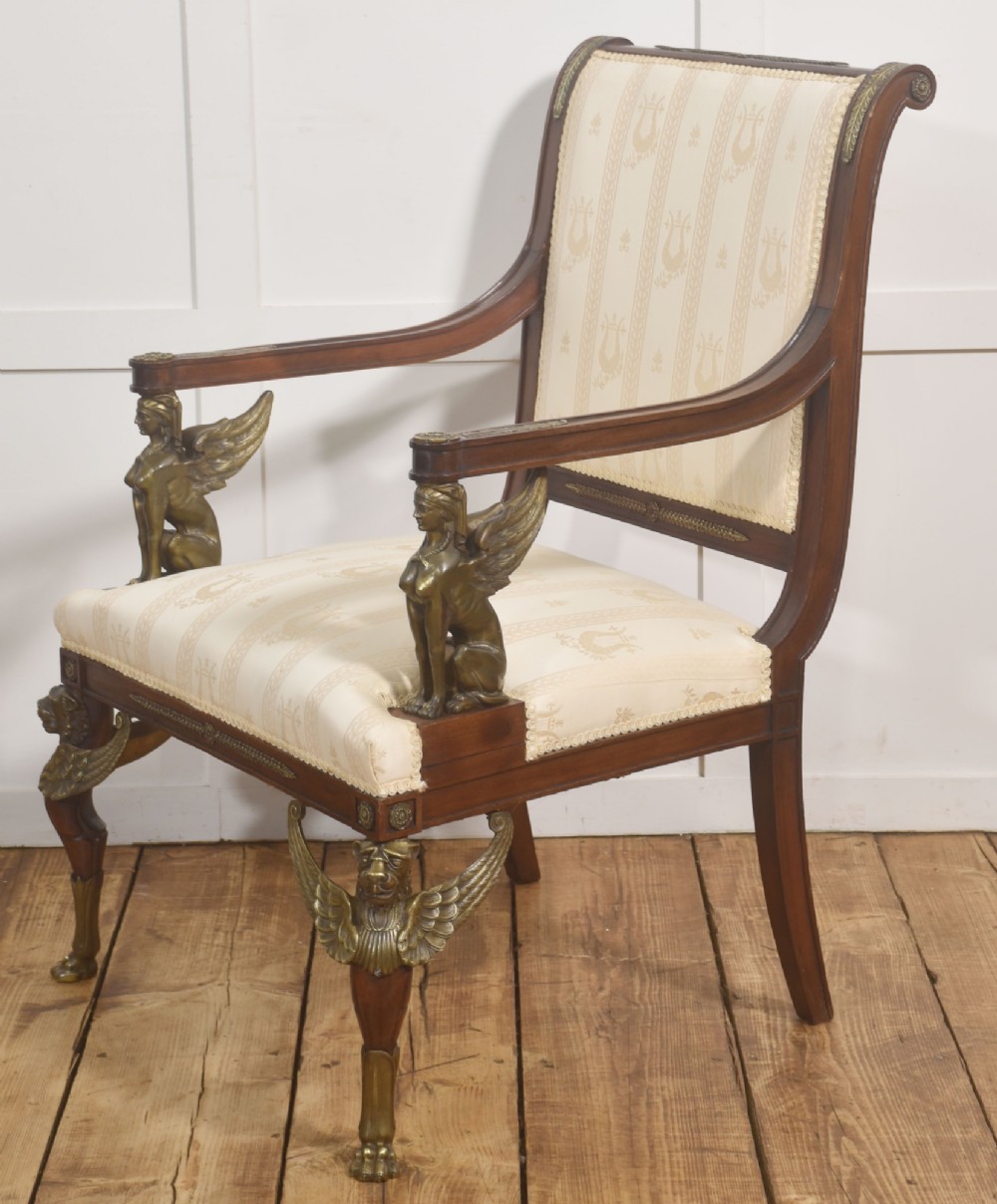 An Empire style mahogany armchair featuring cream upholstered silk fabric with lyre motifs, winged sphinx arm supports, and gilt brass winged lion front legs. View IX