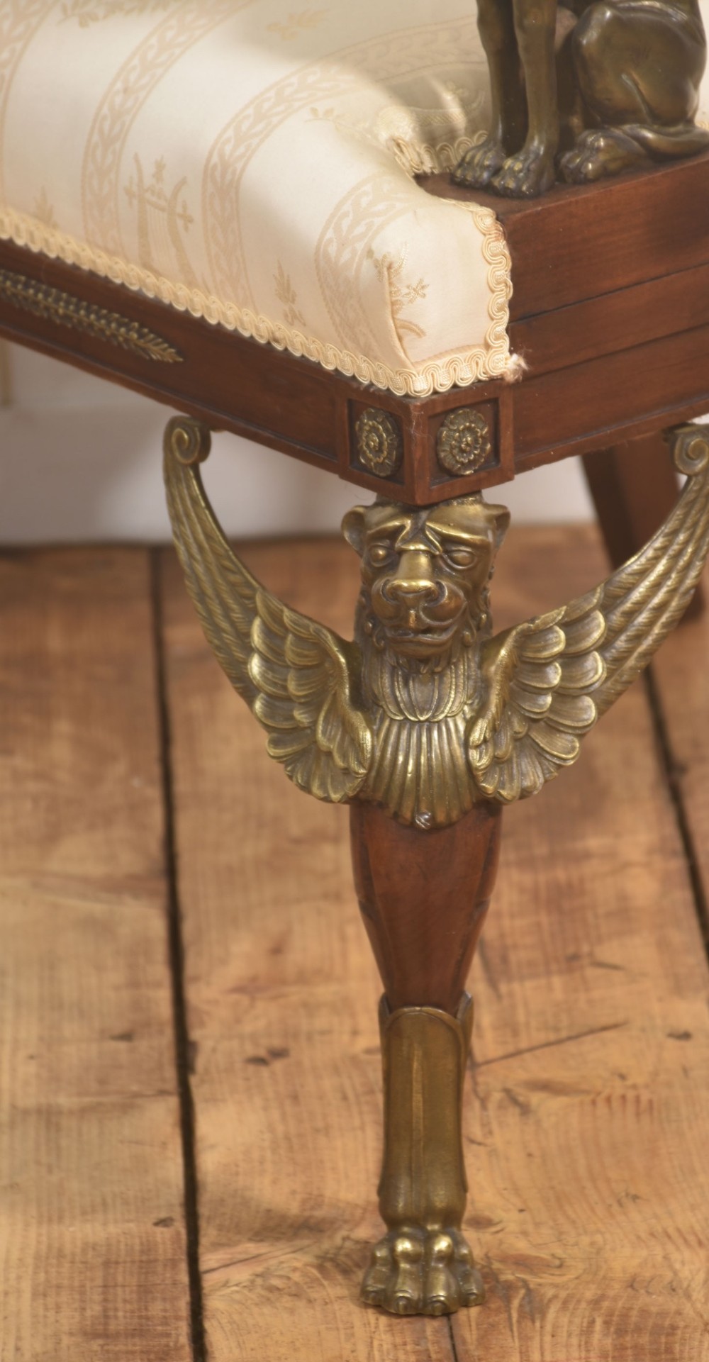 An Empire style mahogany armchair featuring cream upholstered silk fabric with lyre motifs, winged sphinx arm supports, and gilt brass winged lion front legs. View X