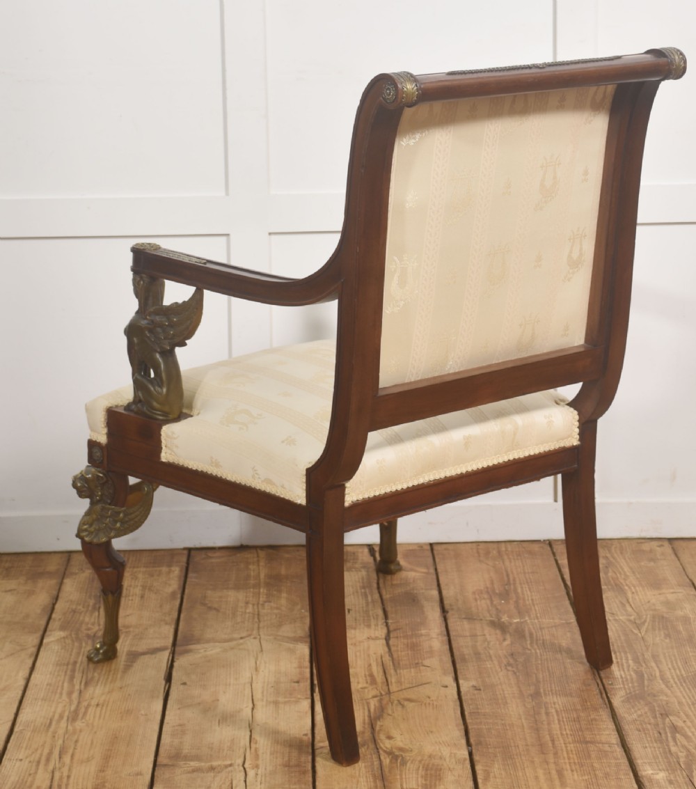 An Empire style mahogany armchair featuring cream upholstered silk fabric with lyre motifs, winged sphinx arm supports, and gilt brass winged lion front legs. View XII