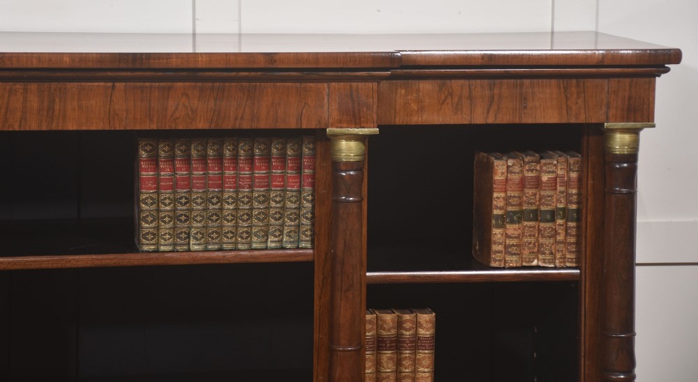 A Regency period open breakfront bookcase crafted from dark rosewood with brass mounted column pilasters and adjustable shelves. View III