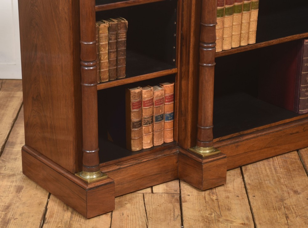 A Regency period open breakfront bookcase crafted from dark rosewood with brass mounted column pilasters and adjustable shelves. View X