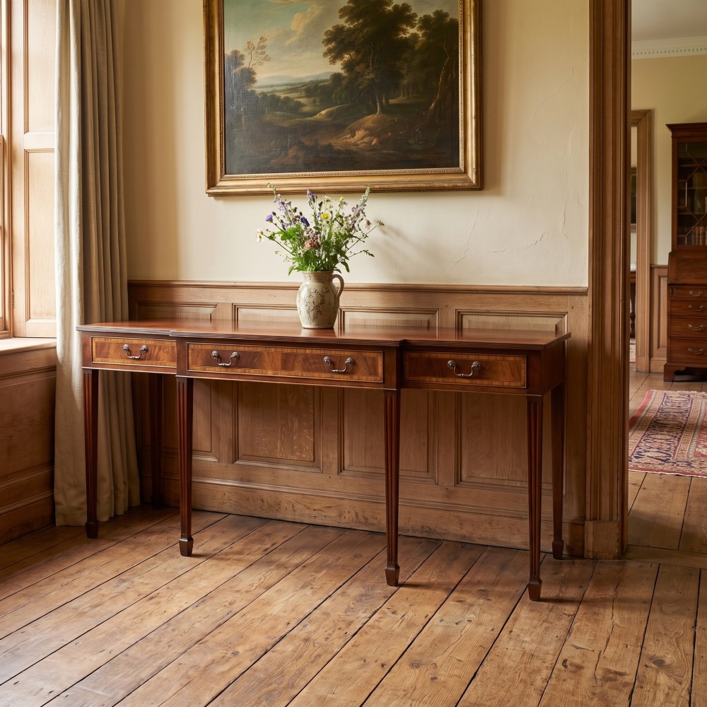 A mahogany breakfront hall table featuring satinwood crossbanding, three drawers with brass handles, and four tapered square legs. View II