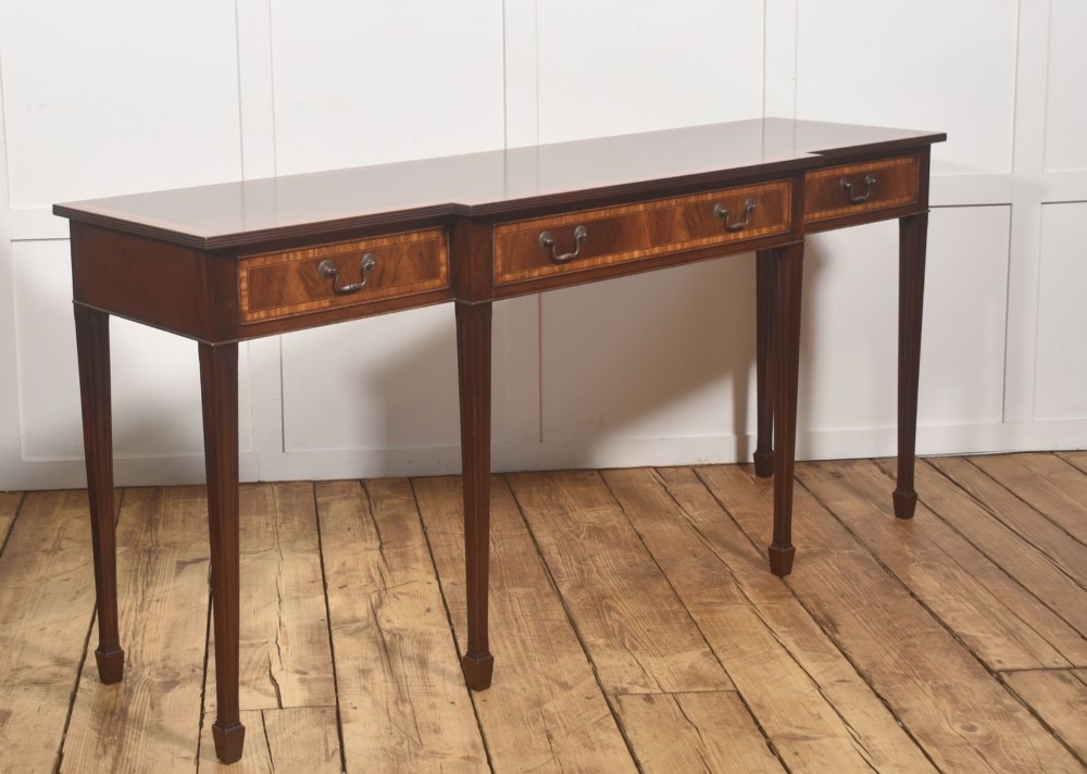 A mahogany breakfront hall table featuring satinwood crossbanding, three drawers with brass handles, and four tapered square legs. View IV