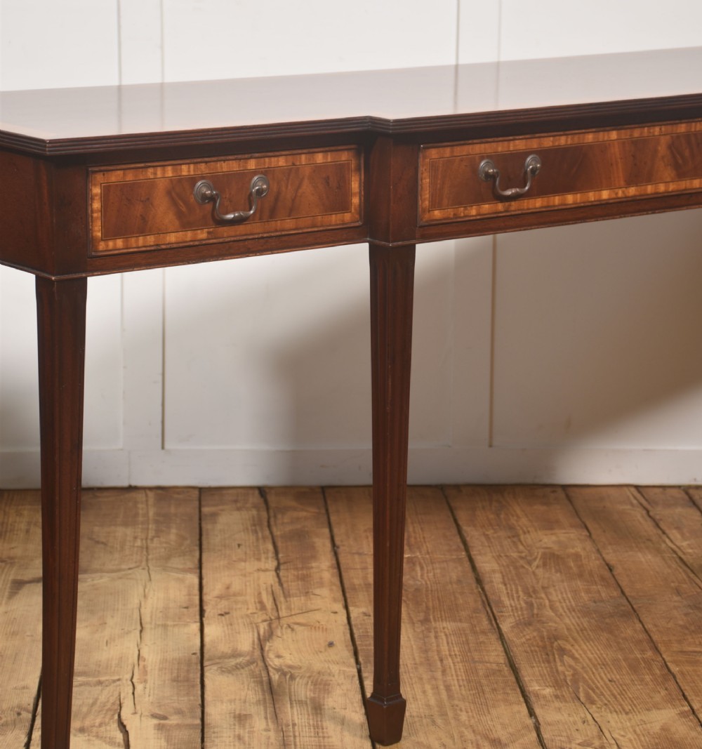 A mahogany breakfront hall table featuring satinwood crossbanding, three drawers with brass handles, and four tapered square legs. View V
