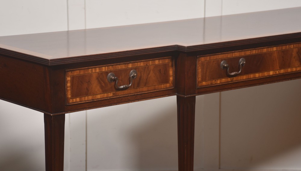 A mahogany breakfront hall table featuring satinwood crossbanding, three drawers with brass handles, and four tapered square legs. View VI