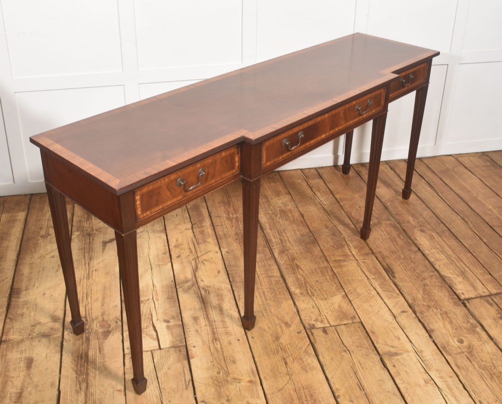 A mahogany breakfront hall table featuring satinwood crossbanding, three drawers with brass handles, and four tapered square legs. View VII