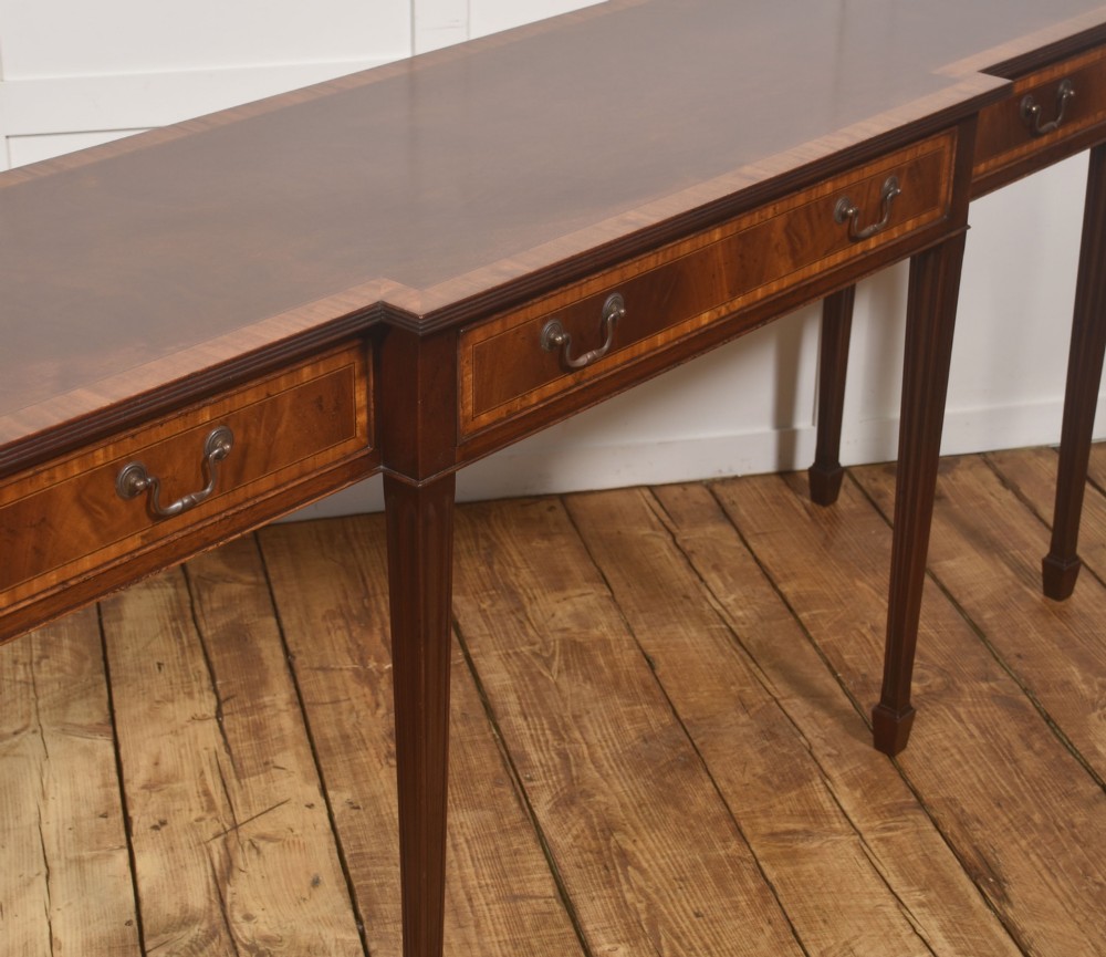 A mahogany breakfront hall table featuring satinwood crossbanding, three drawers with brass handles, and four tapered square legs. View IX