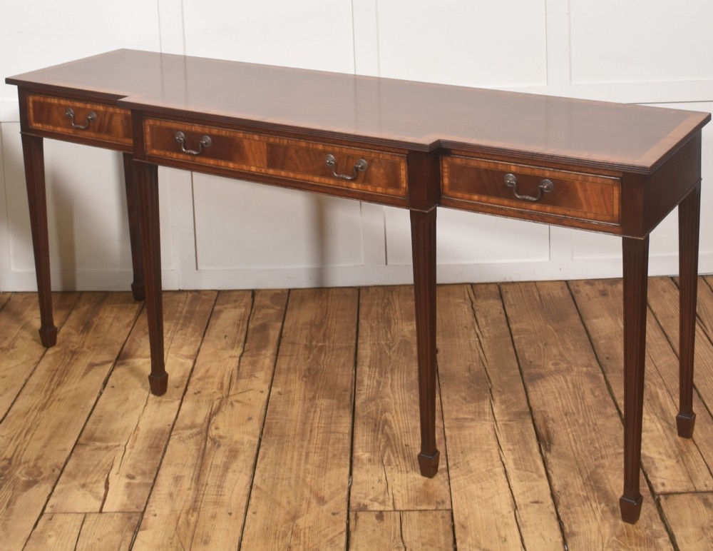 A mahogany breakfront hall table featuring satinwood crossbanding, three drawers with brass handles, and four tapered square legs. View X