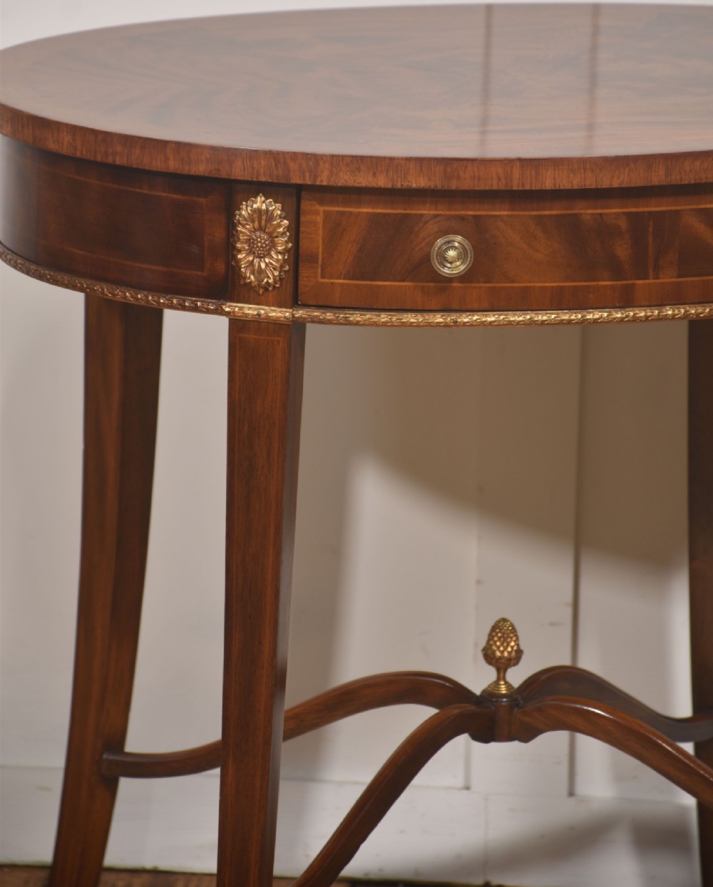 A pair of oval flame mahogany side tables featuring brass rosette mounts, single drawers, curved legs, and an X-shaped stretcher with a brass finial. View IV
