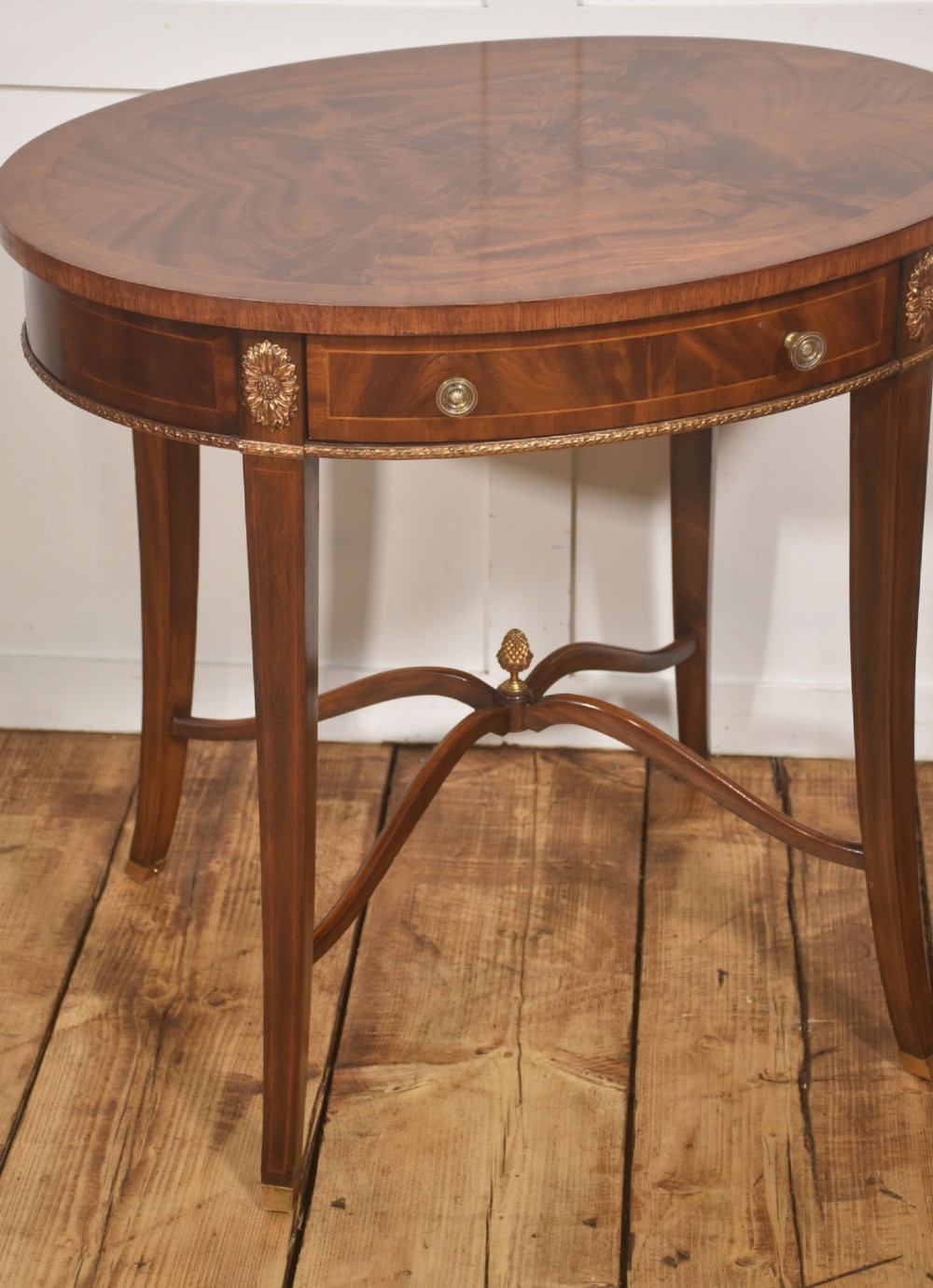 A pair of oval flame mahogany side tables featuring brass rosette mounts, single drawers, curved legs, and an X-shaped stretcher with a brass finial. View VII