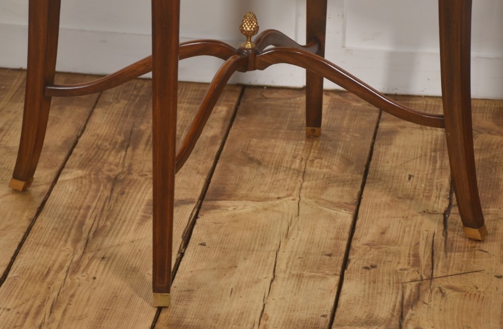 A pair of oval flame mahogany side tables featuring brass rosette mounts, single drawers, curved legs, and an X-shaped stretcher with a brass finial. View X