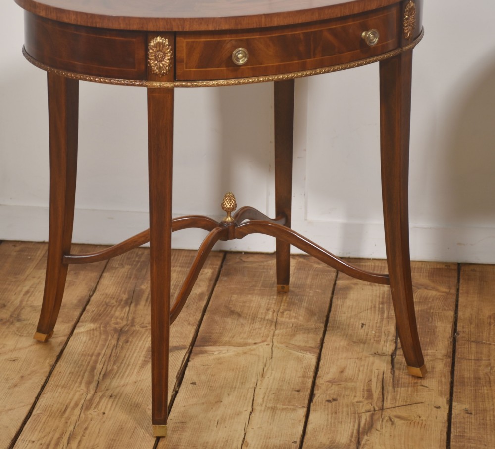 A pair of oval flame mahogany side tables featuring brass rosette mounts, single drawers, curved legs, and an X-shaped stretcher with a brass finial. View XI