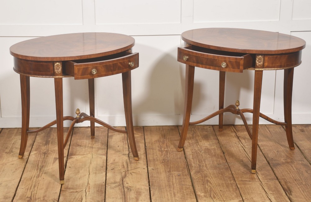 A pair of oval flame mahogany side tables featuring brass rosette mounts, single drawers, curved legs, and an X-shaped stretcher with a brass finial. View XII
