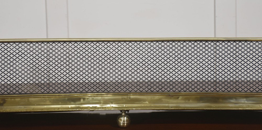 A low rectangular fireplace fender featuring a polished brass top rim and base moulding with black steel diamond mesh sides on small brass ball feet. View VI