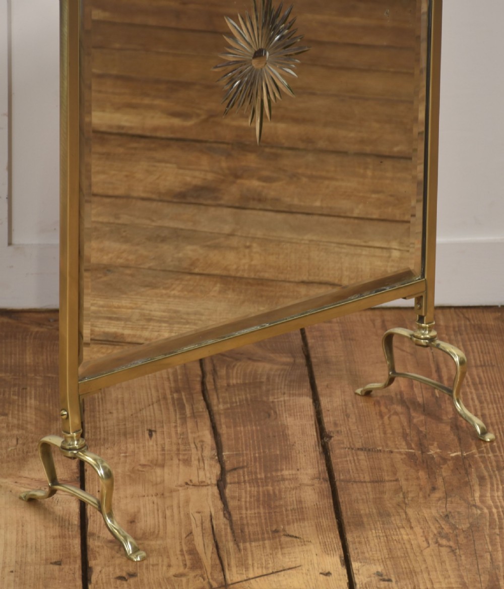 An arched brass-framed fire screen featuring a central cut-glass starburst pattern on a bevelled mirrored panel with a decorative top handle and splayed feet. View III
