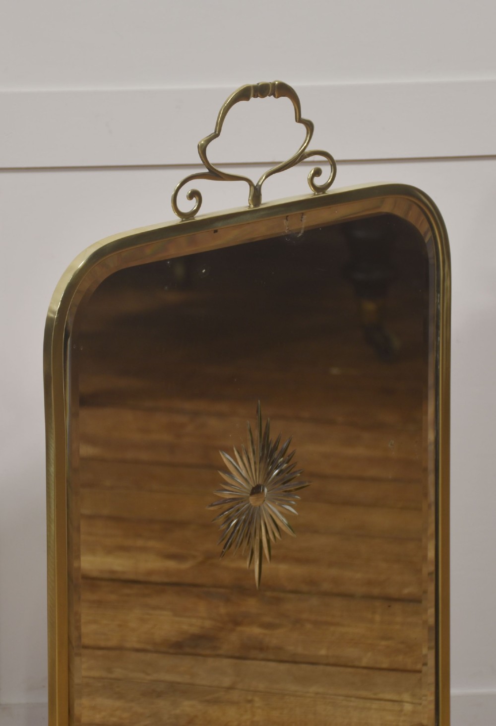 An arched brass-framed fire screen featuring a central cut-glass starburst pattern on a bevelled mirrored panel with a decorative top handle and splayed feet. View IV