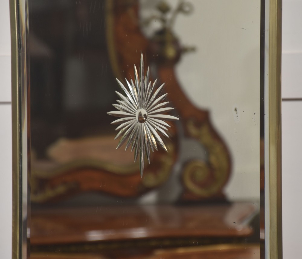An arched brass-framed fire screen featuring a central cut-glass starburst pattern on a bevelled mirrored panel with a decorative top handle and splayed feet. View VI