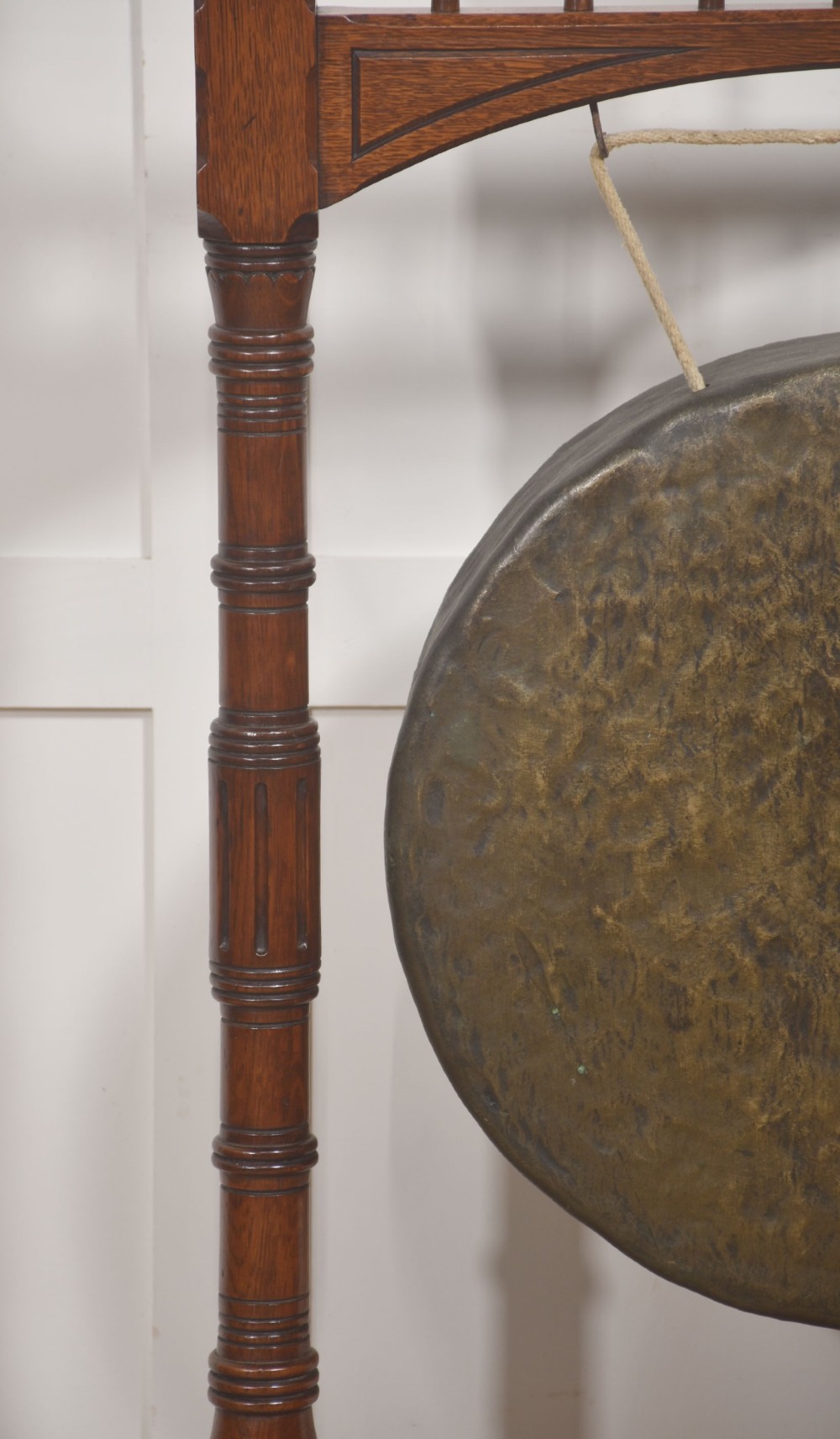 A standing dark oak frame featuring turned upright pillars, top spindles, and a central suspended hammered brass dinner gong dish with a hanging mallet. View IV
