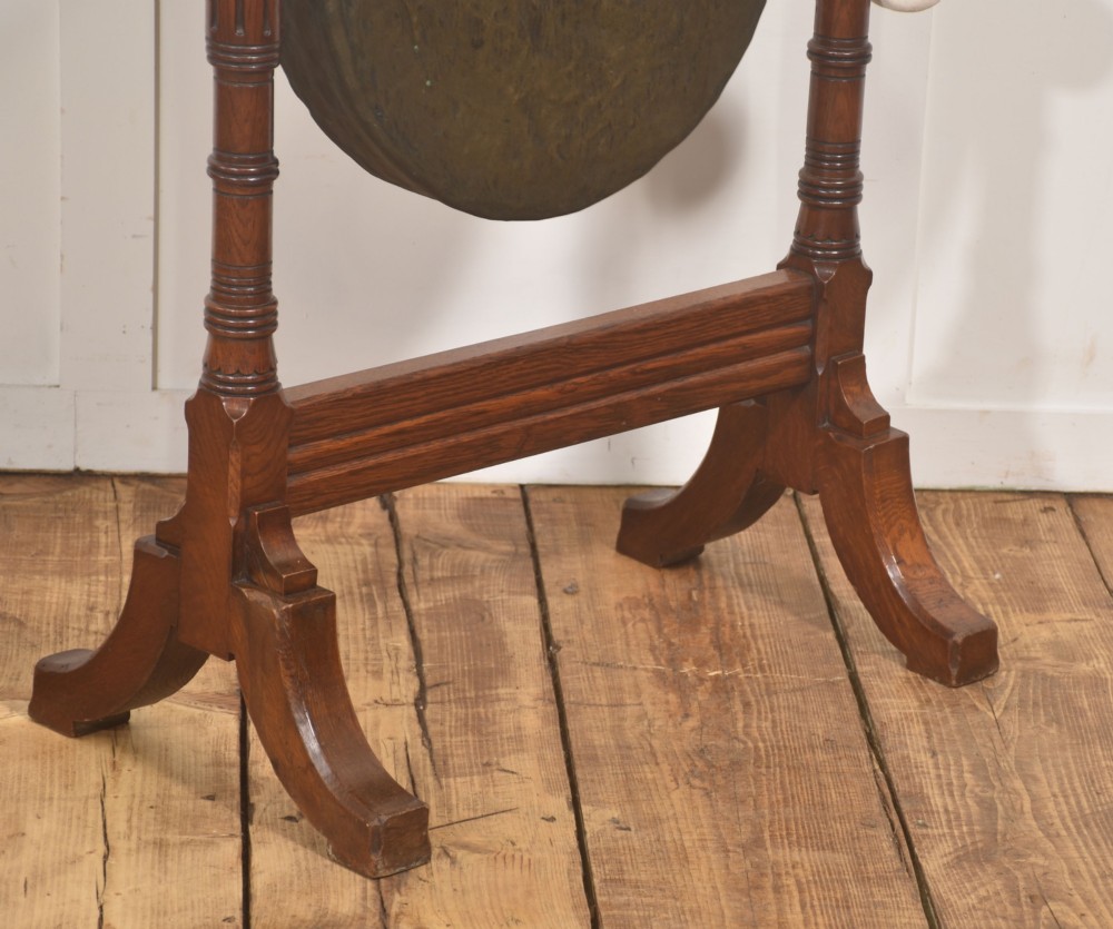 A standing dark oak frame featuring turned upright pillars, top spindles, and a central suspended hammered brass dinner gong dish with a hanging mallet. View VIII