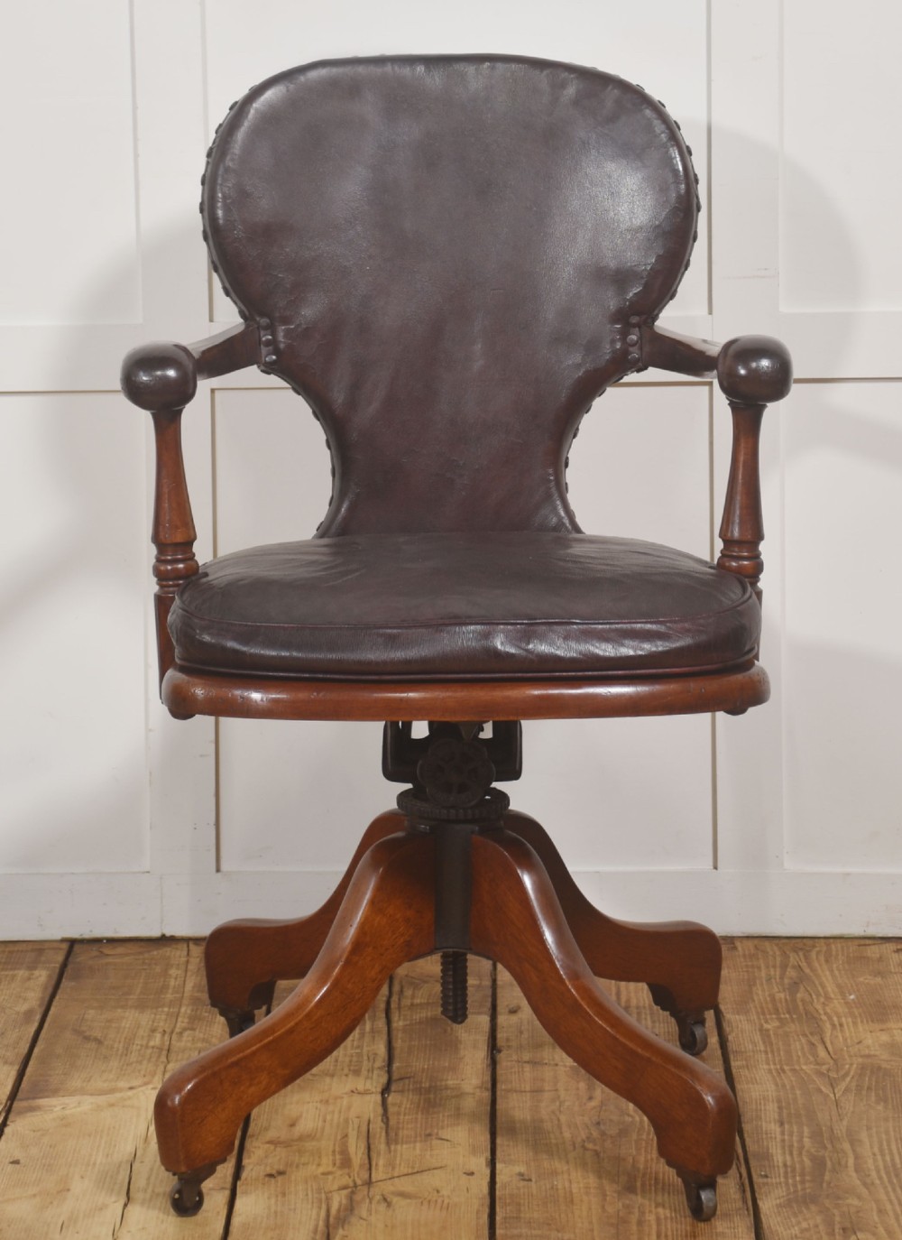 A late Victorian mahogany revolving desk chair upholstered in dark brown leather with turned arm supports and a quadruped base on castors.