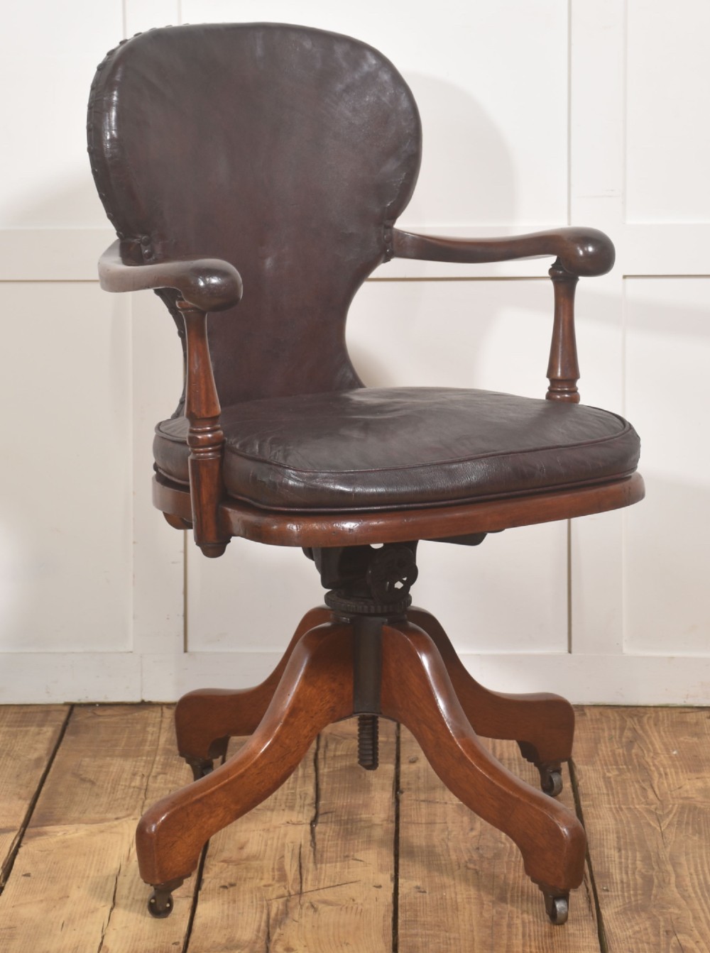 A late Victorian mahogany revolving desk chair upholstered in dark brown leather with turned arm supports and a quadruped base on castors. View III