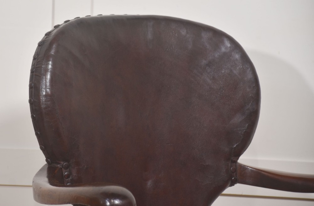A late Victorian mahogany revolving desk chair upholstered in dark brown leather with turned arm supports and a quadruped base on castors. View IV