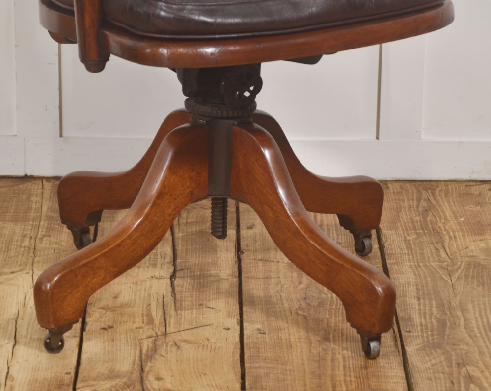 A late Victorian mahogany revolving desk chair upholstered in dark brown leather with turned arm supports and a quadruped base on castors. View V