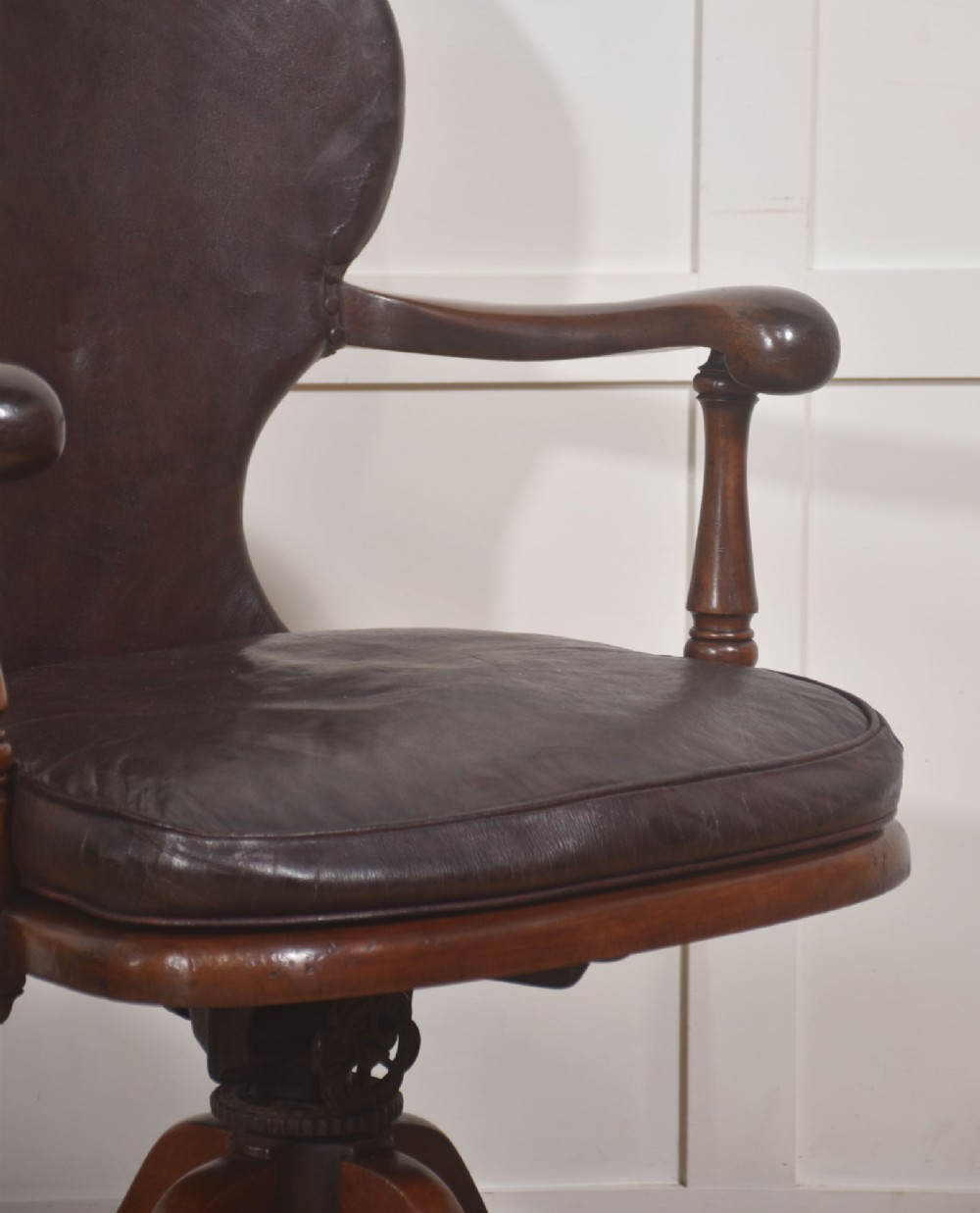 A late Victorian mahogany revolving desk chair upholstered in dark brown leather with turned arm supports and a quadruped base on castors. View VI