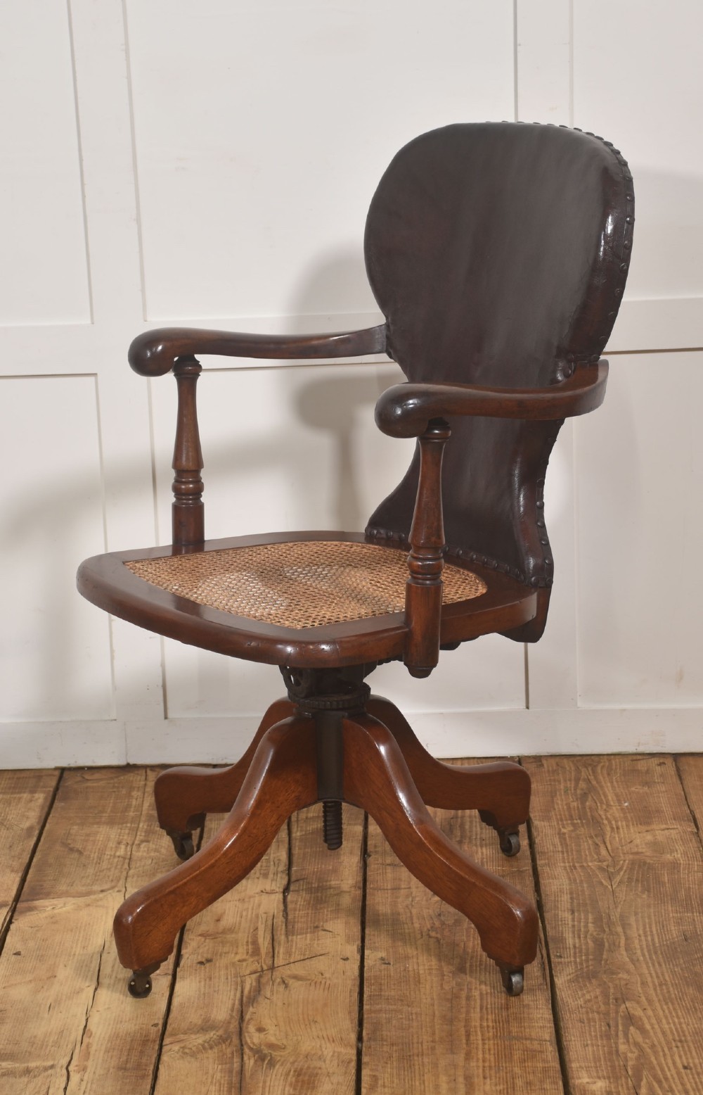 A late Victorian mahogany revolving desk chair upholstered in dark brown leather with turned arm supports and a quadruped base on castors. View VII
