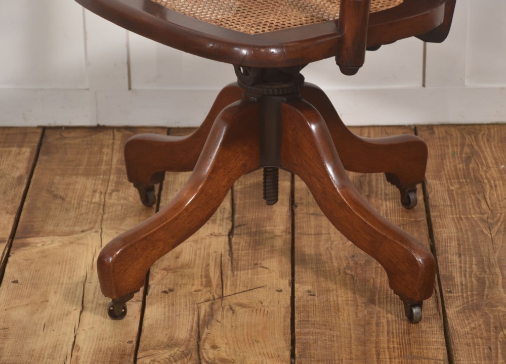 A late Victorian mahogany revolving desk chair upholstered in dark brown leather with turned arm supports and a quadruped base on castors. View VIII