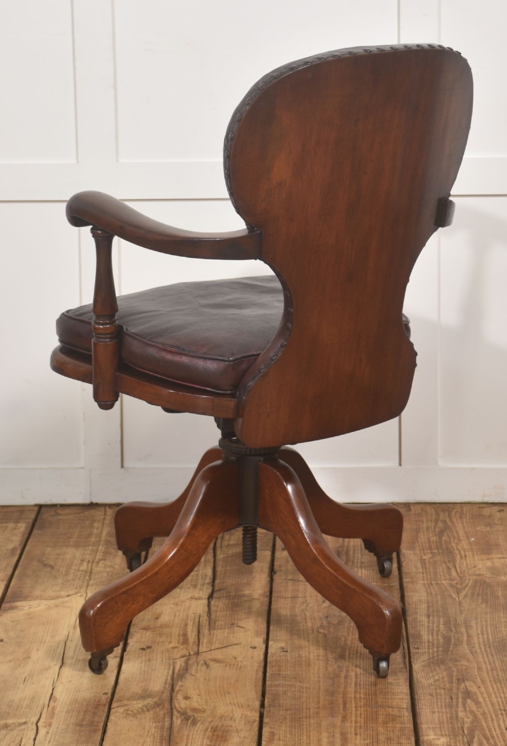 A late Victorian mahogany revolving desk chair upholstered in dark brown leather with turned arm supports and a quadruped base on castors. View IX