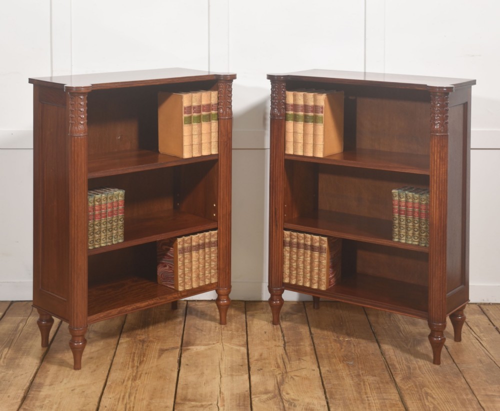 A pair of low mahogany open bookcases featuring fluted pilasters with carved tops, adjustable shelves, and turned legs.