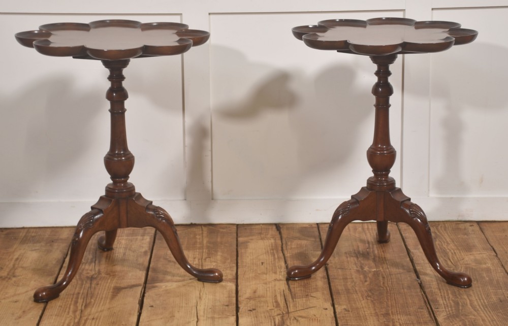 A pair of polished dark mahogany tripod side tables featuring scalloped pie-crust tops, turned central pedestals, and carved cabriole legs.