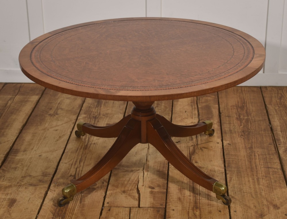 A circular Regency style mahogany coffee table featuring an inset brown leather top with gold leaf tooling, supported by a central pedestal and four splayed legs fitted with brass castors.