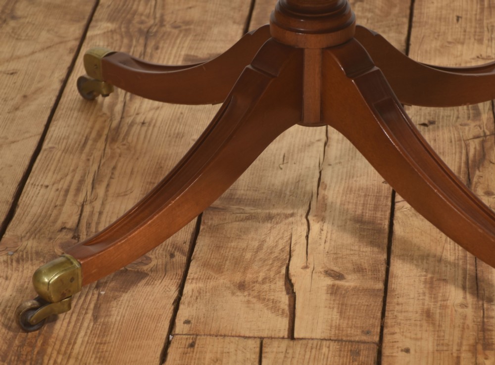 A circular Regency style mahogany coffee table featuring an inset brown leather top with gold leaf tooling, supported by a central pedestal and four splayed legs fitted with brass castors. View IV
