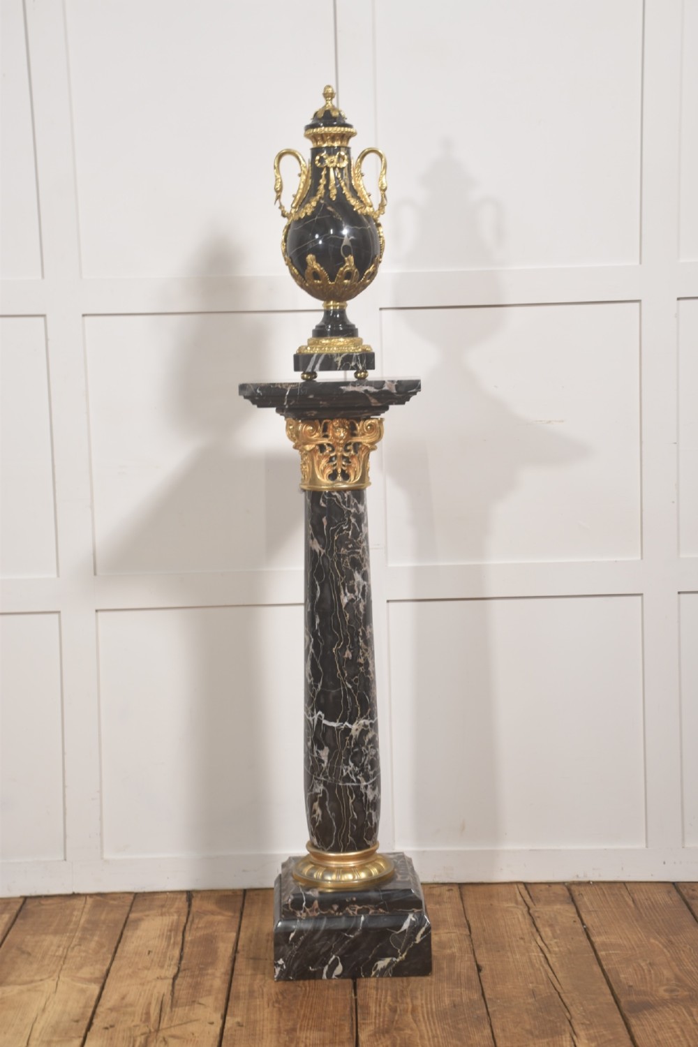 A black veined-marble urn with two handles and gilt-metal mounts resting on a matching cylindrical black marble pedestal with a Corinthian capital.