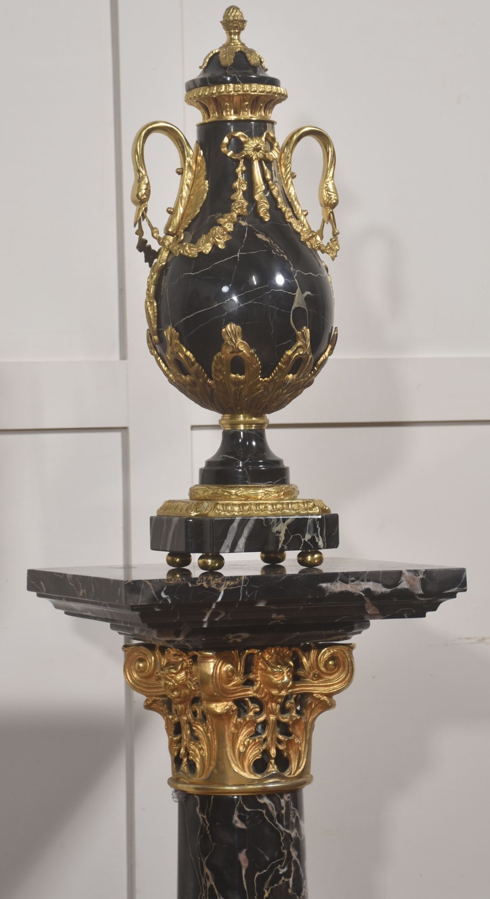 A black veined-marble urn with two handles and gilt-metal mounts resting on a matching cylindrical black marble pedestal with a Corinthian capital. View IV