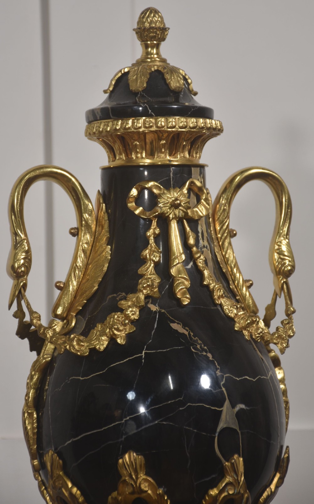 A black veined-marble urn with two handles and gilt-metal mounts resting on a matching cylindrical black marble pedestal with a Corinthian capital. View V