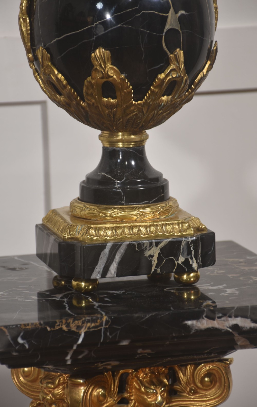 A black veined-marble urn with two handles and gilt-metal mounts resting on a matching cylindrical black marble pedestal with a Corinthian capital. View VI