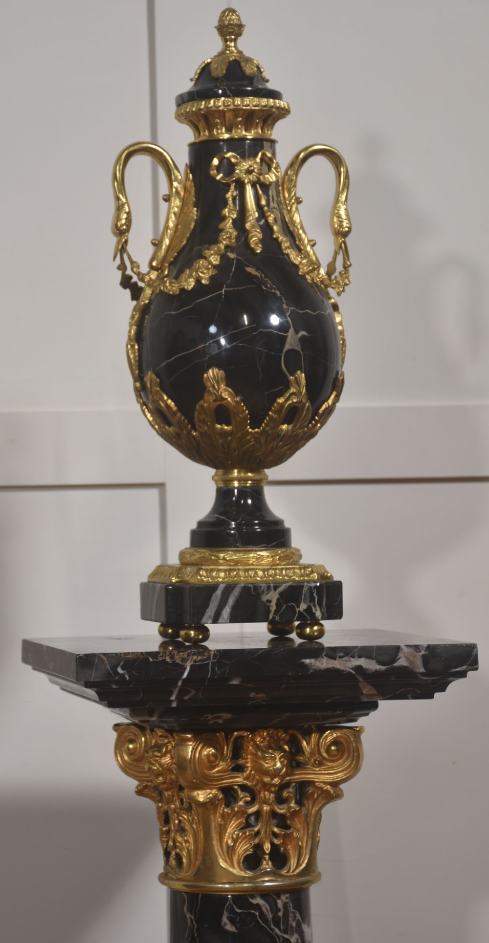A black veined-marble urn with two handles and gilt-metal mounts resting on a matching cylindrical black marble pedestal with a Corinthian capital. View VIII