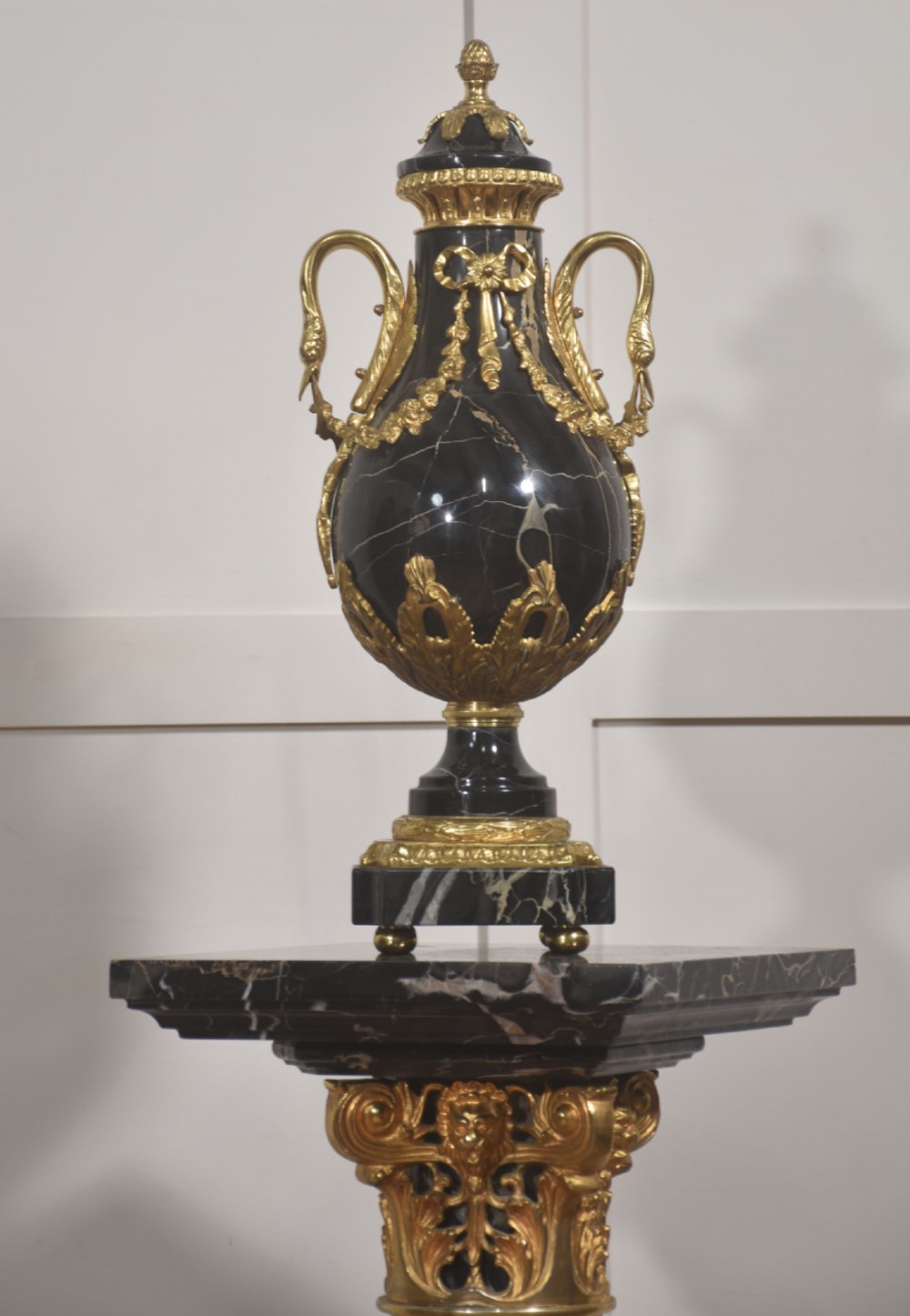 A black veined-marble urn with two handles and gilt-metal mounts resting on a matching cylindrical black marble pedestal with a Corinthian capital. View X