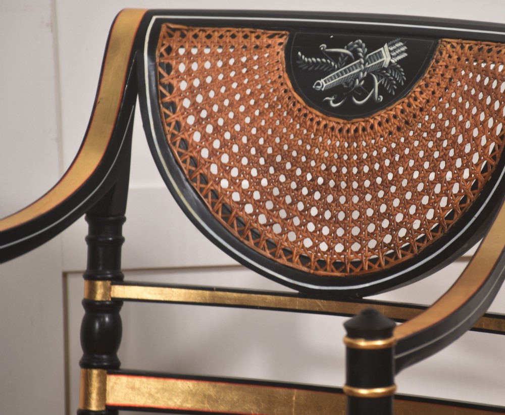 A Regency style ebonised and parcel-gilt open armchair featuring a curved cane backrest with painted medallion detail, sweeping arms, and a patterned gold upholstered cushion. View III