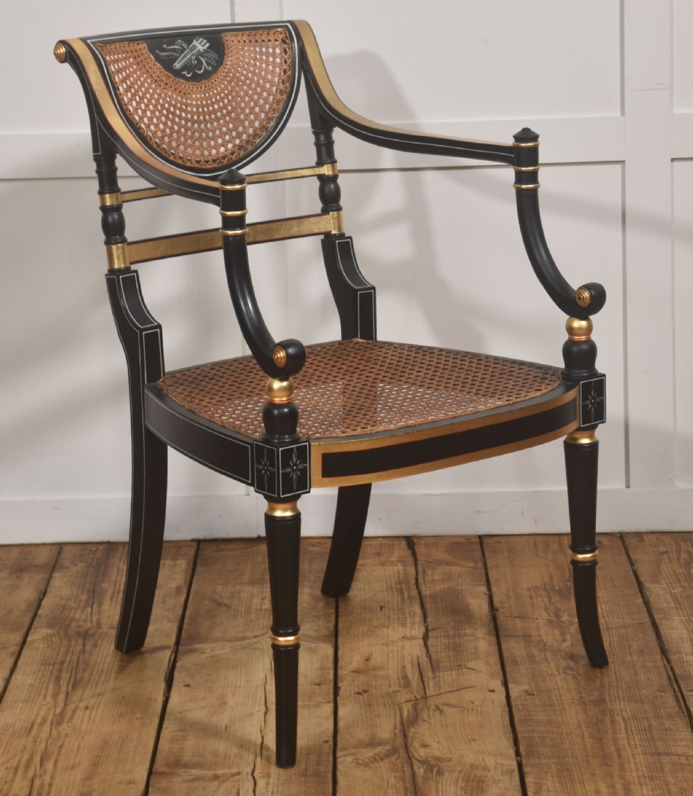 A Regency style ebonised and parcel-gilt open armchair featuring a curved cane backrest with painted medallion detail, sweeping arms, and a patterned gold upholstered cushion. View VII