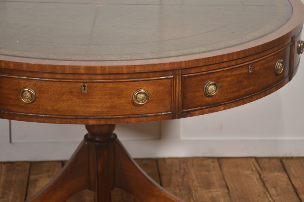 A circular mahogany drum table featuring a green leather top with gold tooling, multiple drawers with brass ring handles, and a four-legged pedestal base on castors. View III