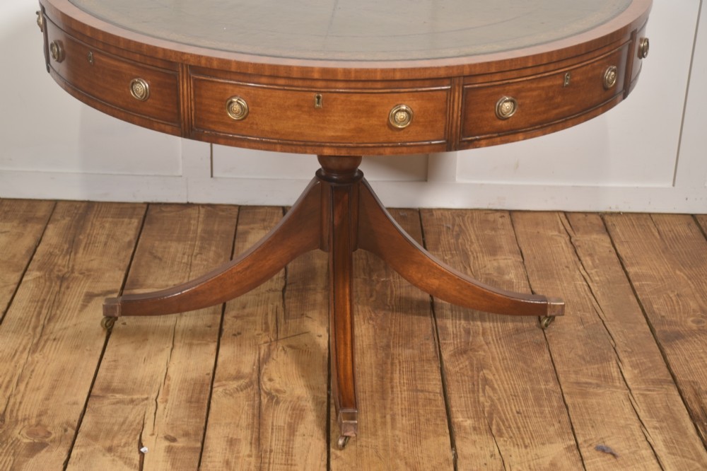 A circular mahogany drum table featuring a green leather top with gold tooling, multiple drawers with brass ring handles, and a four-legged pedestal base on castors. View IV