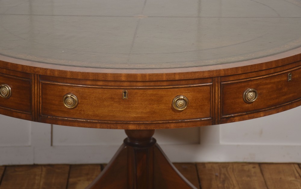 A circular mahogany drum table featuring a green leather top with gold tooling, multiple drawers with brass ring handles, and a four-legged pedestal base on castors. View V