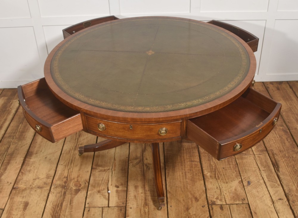 A circular mahogany drum table featuring a green leather top with gold tooling, multiple drawers with brass ring handles, and a four-legged pedestal base on castors. View VI