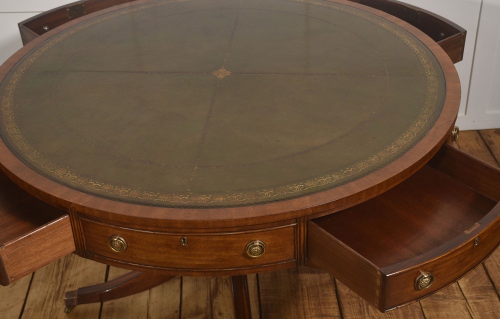 A circular mahogany drum table featuring a green leather top with gold tooling, multiple drawers with brass ring handles, and a four-legged pedestal base on castors. View VII